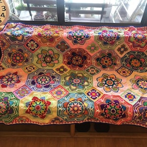 May include: A vibrant, hand-crocheted blanket with a floral design. The blanket showcases a spectrum of colours, such as pink, green, yellow, and purple. Crafted from soft yarn, it's ideal for cosy moments. The blanket measures approximately 152 cm by 203 cm.