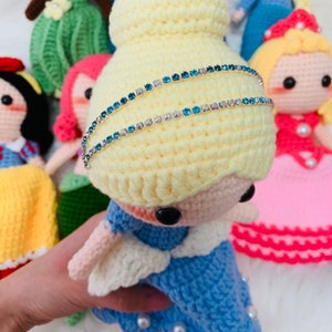 Peut inclure: Une poup&eacute;e en crochet avec des cheveux blonds et une robe bleue. La poup&eacute;e porte un bandeau bleu scintillant.