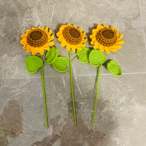 May include: Three crocheted sunflowers with green leaves. The sunflowers are yellow with brown centers. The leaves are a bright green.
