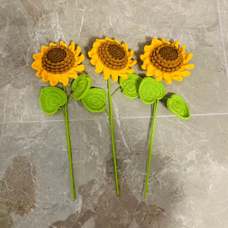 May include: Three crocheted sunflowers with green leaves. The sunflowers are yellow with brown centers. The leaves are a bright green.