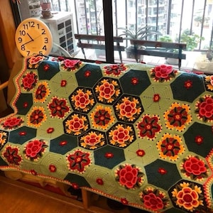May include: A handmade crochet blanket with a floral pattern. The blanket features a repeating design of hexagonal shapes in shades of teal, green, and red, with yellow and orange flower details. The blanket is draped over a sofa.