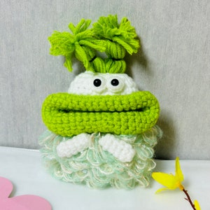 Può includere: Un giocattolo di peluche verde all'uncinetto con pelliccia bianca e grandi occhi neri. Il giocattolo ha una grande bocca verde e capelli verdi.
