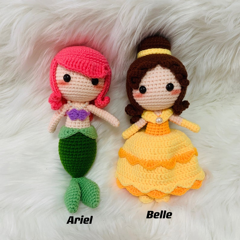 Peut inclure: Deux poup&eacute;es en crochet, l'une avec une queue de sir&egrave;ne rose et verte et l'autre avec une robe jaune. La poup&eacute;e sir&egrave;ne porte un soutien-gorge en coquillage violet et un collier de perles. La poup&eacute;e avec la robe jaune a un chignon brun et un collier de perles. Les poup&eacute;es sont &eacute;tiquet&eacute;es "Ariel" et "Belle".