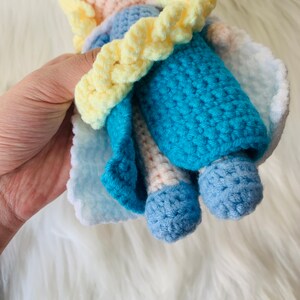 Puede incluir: Una mu&ntilde;eca de crochet con un vestido azul, un cintur&oacute;n de crochet amarillo y una capa de crochet blanca.