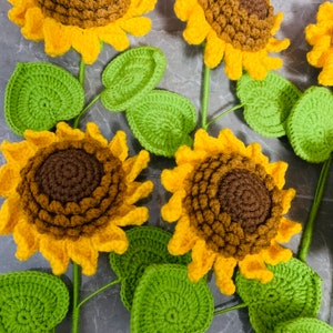 May include: A set of crocheted sunflowers with green leaves. The sunflowers are yellow with brown centers and the leaves are a bright green.