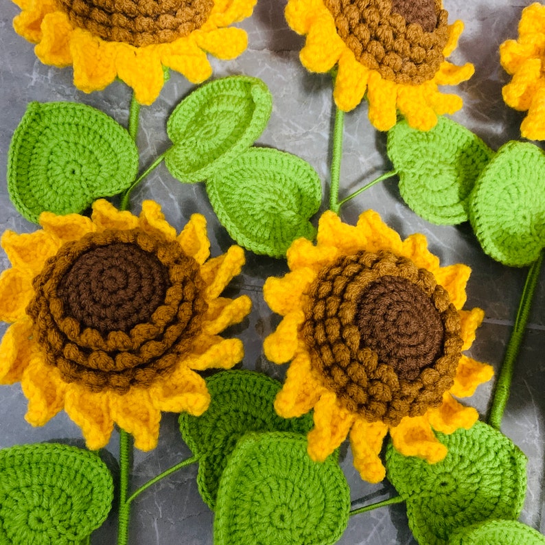 May include: A set of crocheted sunflowers with green leaves. The sunflowers are yellow with brown centers and the leaves are a bright green.