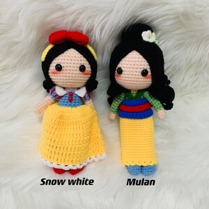 Peut inclure: Deux poup&eacute;es en crochet, Blanche-Neige et Mulan, sont habill&eacute;es dans leurs tenues embl&eacute;matiques. Blanche-Neige porte une robe jaune avec un corsage bleu et un n&oelig;ud rouge. Mulan porte une robe jaune avec un corsage vert et rouge. Les deux poup&eacute;es ont les cheveux noirs et de grands yeux expressifs.