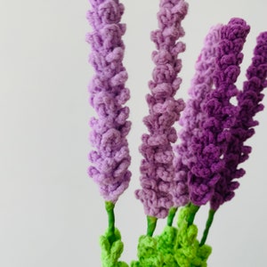May include: A bunch of purple and lavender crocheted lavender flowers with green stems.