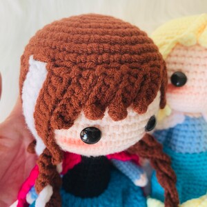 Puede incluir: Dos mu&ntilde;ecas de crochet, una con cabello casta&ntilde;o y un vestido azul, la otra con cabello rubio y un vestido azul.
