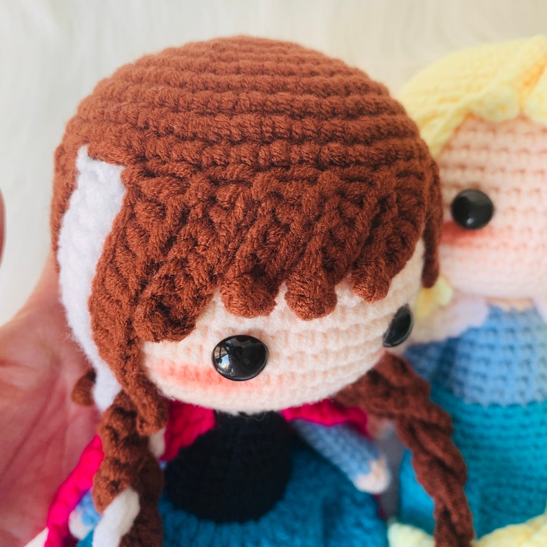Puede incluir: Dos mu&ntilde;ecas de crochet, una con cabello casta&ntilde;o y un vestido azul, la otra con cabello rubio y un vestido azul.