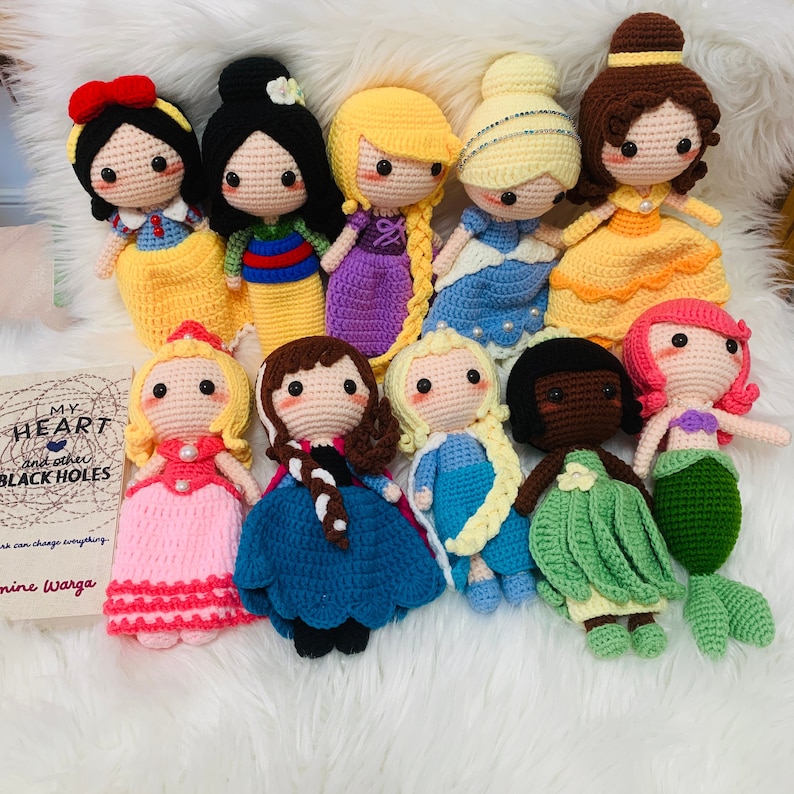 Peut inclure: Une collection de 11 poup&eacute;es princesses Disney en crochet. Les poup&eacute;es portent toutes leurs robes caract&eacute;ristiques et ont des traits du visage d&eacute;taill&eacute;s. Les poup&eacute;es sont dispos&eacute;es en cercle sur une surface blanche et moelleuse.