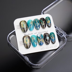 May include: A set of ten false nails with different designs featuring turquoise, gold, and black colors. The nails are displayed in a clear plastic case with a white card that reads "Handmade nail enhancement".
