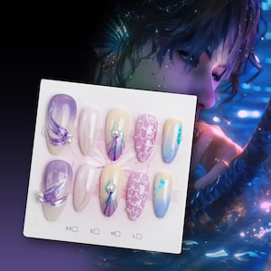 May include: A set of ten false nails with different designs. The nails are in various shades of purple, blue, and white. Some nails have a mermaid scale design, while others have a pearl and feather design. The nails are arranged on a white card with the sizes XS, S, M, and L labelled.