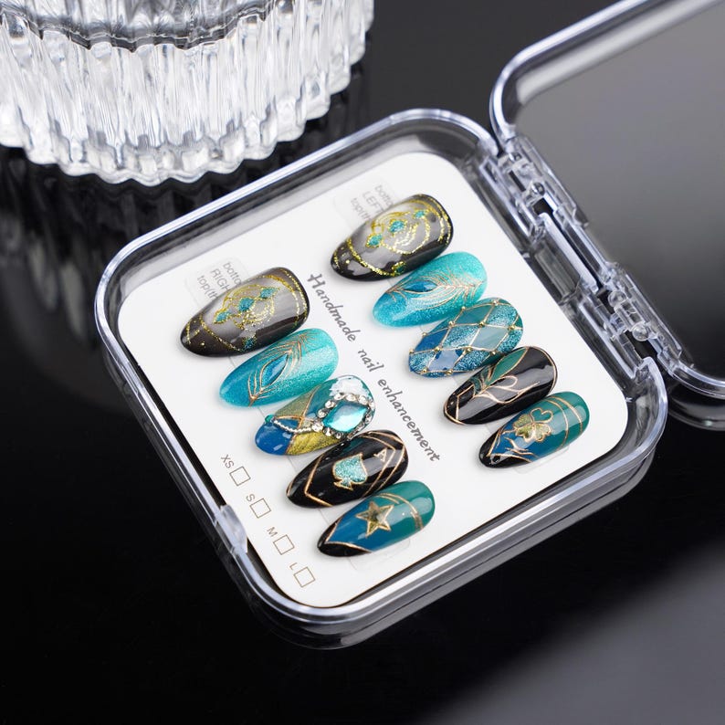 May include: A set of ten false nails with intricate designs featuring blue, green, gold, and black colors. The nails are arranged in a clear plastic case with a white card that reads "Handmade nail enhancement".