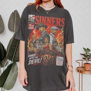 Puede incluir: Una camiseta gris carbón con un estampado gráfico de estilo vintage con el texto SINNERS, DANCE WITH THE DEVIL, 18 APR 2025, y BLOOD, BROTHERHOOD, REDEMPTION. THE PAST ALWAYS COLLECTS. El diseño muestra varias figuras en un entorno ardiente.