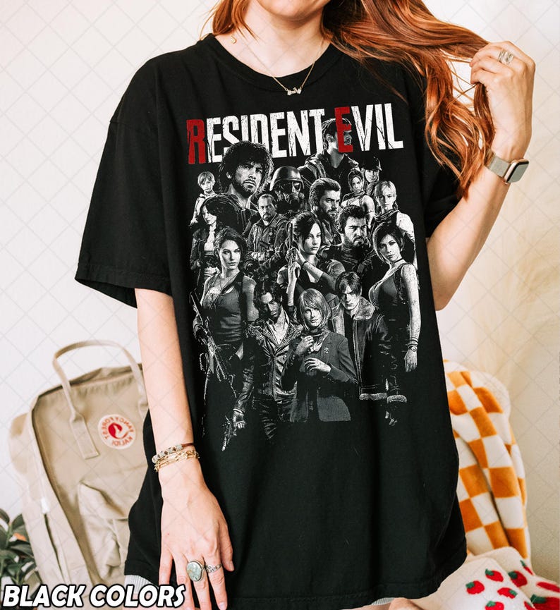 May include: Black t-shirt featuring a group of characters from the video game "Resident Evil" in a grayscale graphic. The title "RESIDENT EVIL" is printed across the top in red and white letters. The words "BLACK COLORS" are printed at the bottom.