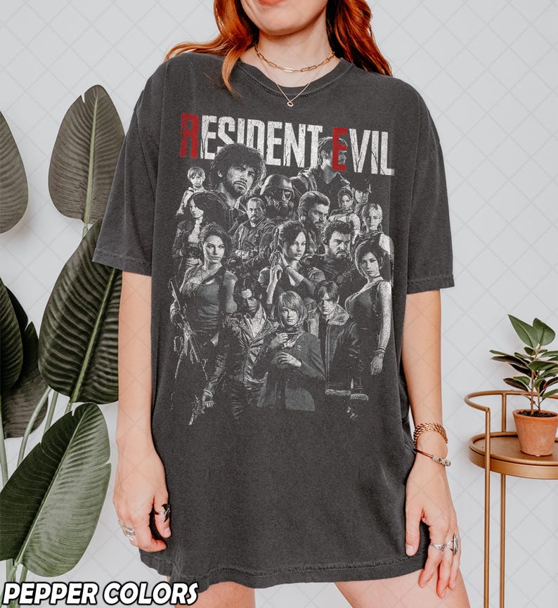 May include: Dark gray t-shirt featuring a group of characters from the Resident Evil video game series. The text "RESIDENT EVIL" is printed across the top in red and white. The shirt is from Pepper Colors.