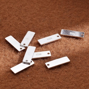 Può includere: Un set di dieci etichette rettangolari in metallo color argento con angoli arrotondati. Ogni etichetta ha un foro nella parte superiore per attaccare una corda o una catena. Le etichette sono vuote, pronte per essere personalizzate.