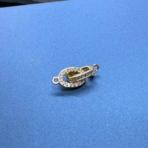 Op de afbeelding: Gouden metalen sluiting met heldere kristallen versieringen. De sluiting is ontworpen om twee sieraden te verbinden.