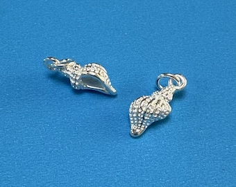 Könnte beinhalten: Zwei silberne Muschel-Anhänger mit strukturierter Oberfläche. Die Anhänger sind perfekt, um Schmuck mit einem Hauch von nautischem Stil zu versehen.