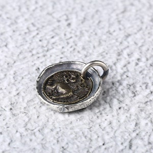 May include: Silver pendant with a round, textured frame and a circular coin featuring a profile of a person. The coin is slightly raised from the frame.