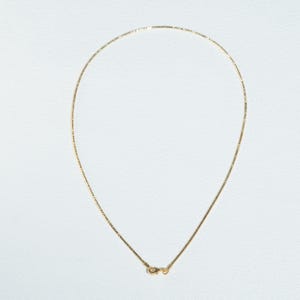 Könnte beinhalten: Eine zarte goldene Halskette mit feiner Kette und kleinem Verschluss. Die Halskette wird vor einem weißen Hintergrund präsentiert, was ihre schlichte Eleganz unterstreicht. Die Kette ist etwa 40 cm lang.