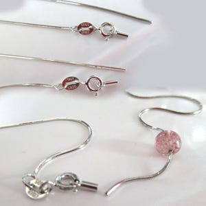 May include: Close-up of several silver necklaces and earring components. The necklaces have delicate, thin chains with lobster claw clasps. One earring features a pink, round bead. The clasps are marked with "ITALY S925" and "925 KOREA".