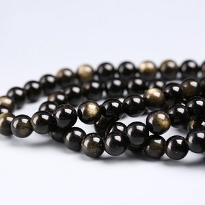 May include: A strand of black beads with gold flecks. The beads are round and smooth, and they are strung together on a clear thread.