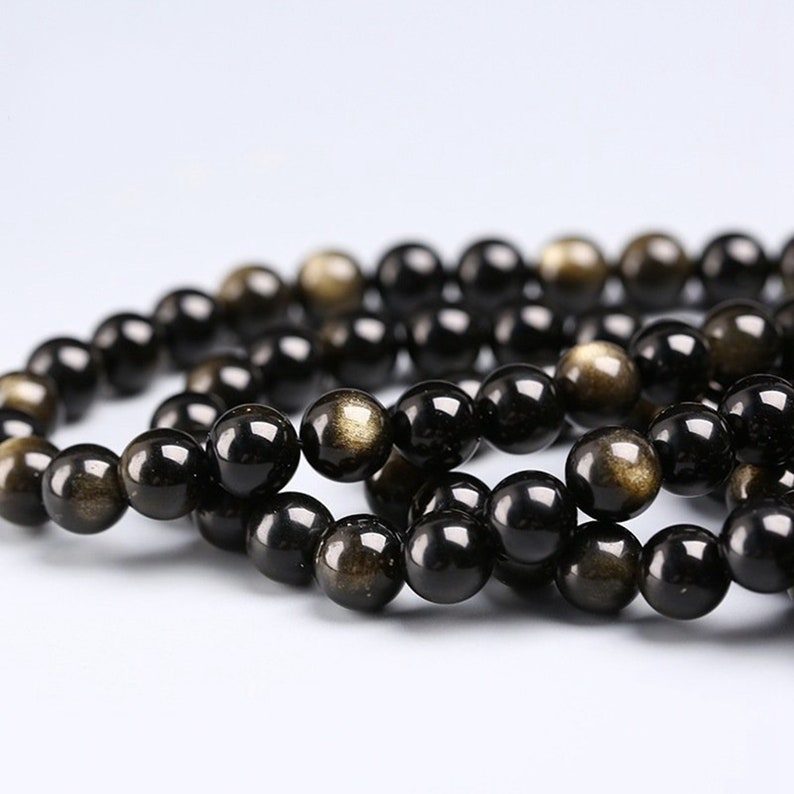 May include: A strand of black beads with gold flecks. The beads are round and smooth, and they are strung together on a clear thread.