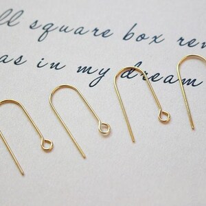 May include: Five gold-toned earring hooks, each with a small loop at the end. The hooks are arranged in a row on a white surface.
