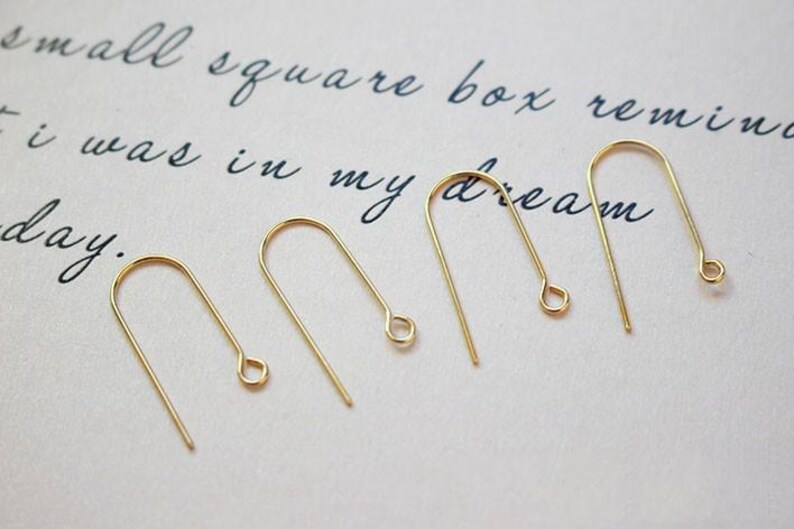 May include: Five gold-toned earring hooks, each with a small loop at the end. The hooks are arranged in a row on a white surface.