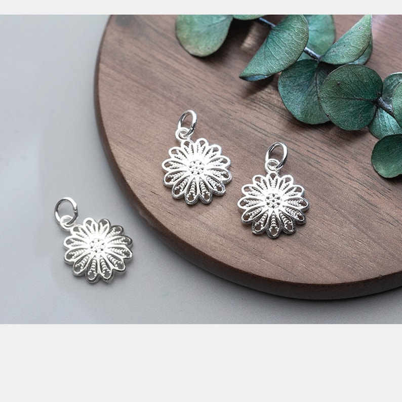 May include: Three silver filigree flower charms with a loop for attaching to a necklace or bracelet.