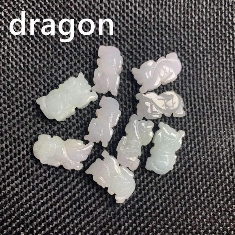 Pode incluir: Uma cole&ccedil;&atilde;o de pequenas figuras de drag&atilde;o de jade esculpido em tons de verde p&aacute;lido e lavanda. A palavra "drag&atilde;o" est&aacute; impressa em branco no topo. As figuras est&atilde;o dispostas sobre uma superf&iacute;cie escura e texturizada.