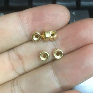 May include: Five gold-colored metal beads with a hole in the center. The beads are round and have a slightly raised edge.