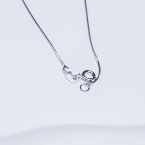 Op de afbeelding: Close-up van een zilveren ketting met een fijne ketting. De sluiting en het uiteinde van de ketting zijn zichtbaar, met de sluiting gemarkeerd met "ITALY 925". De ketting staat tegen een witte achtergrond.