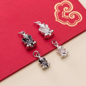 May include: Four silver charms in the shape of an elephant, each with intricate details. The charms are on a red background.