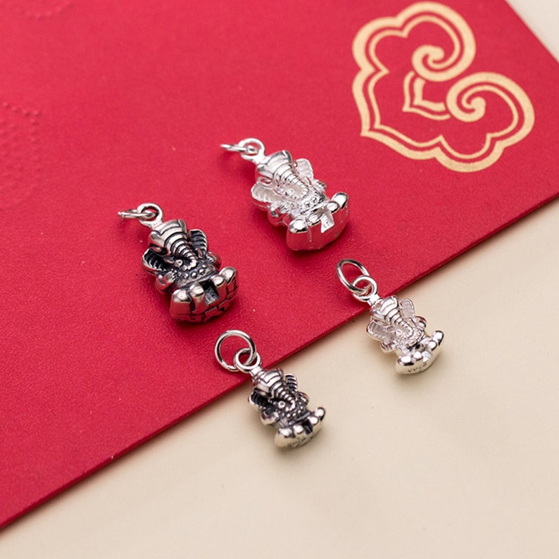 May include: Four silver charms in the shape of an elephant, each with intricate details. The charms are on a red background.