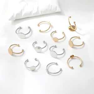 May include: A collection of ten open-ended rings featuring flat circular pads for jewelry making. The set includes five silver-toned rings and five gold-toned rings, each with a small ball at both ends of the band for a secure and adjustable fit.