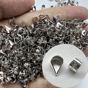 May include: A selection of small, shiny silver-coloured jewellery findings, including teardrop-shaped bails and other connector pieces. The pieces are scattered, with a close-up of a teardrop bail and a small rectangular bail with "S92" stamped on it.