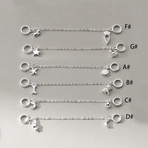 May include: A selection of silver charm bracelets, each with a unique pendant. Charms include a rabbit, moon, bell, dog, seashell, starfish, star, and carrot. Each bracelet has a chain and two circular clasps. The letters F#, G#, A#, B#, C#, and D# are printed on the right side.