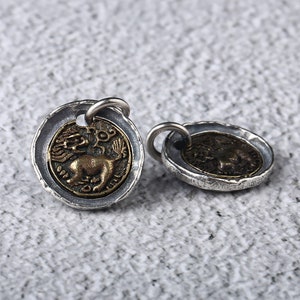 May include: Two silver and gold tone pendants featuring a lion design. The pendants have a textured edge and a loop for attaching to a chain.