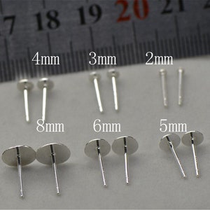 Peut inclure: Assortiment de tiges d'oreilles en argent de diff&eacute;rentes tailles, notamment 2 mm, 3 mm, 4 mm, 5 mm, 6 mm et 8 mm. Les tiges d'oreilles sont pr&eacute;sent&eacute;es sur une surface blanche avec une r&egrave;gle en arri&egrave;re-plan.