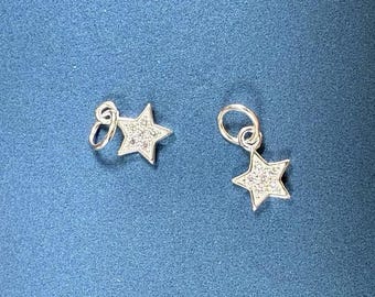 May include: Two silver star-shaped charms with clear crystal accents. The charms have a loop at the top for attaching to a bracelet or necklace.