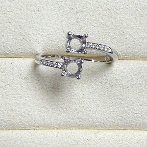 May include: A silver ring with two open settings for stones, surrounded by small clear stones.