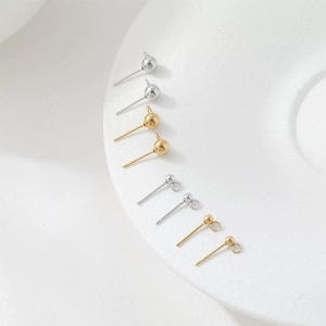 May include: A collection of six metal stud earrings arranged in a vertical line. The set includes two silver-toned ball studs, two gold-toned ball studs, and two silver-toned and gold-toned ball studs each featuring a small attached jump ring.