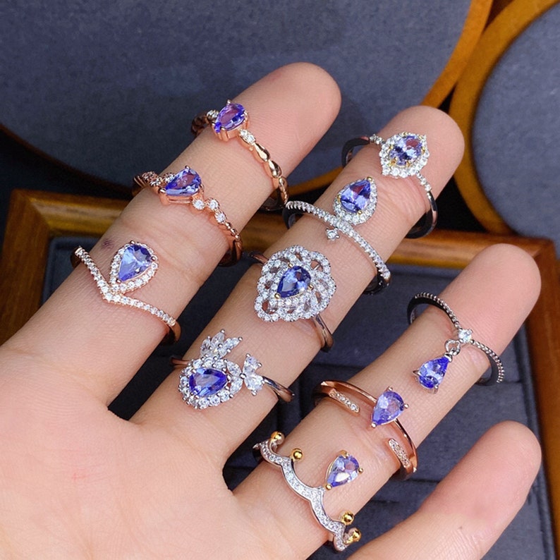 May include: A collection of silver rings featuring blue pear-shaped gemstones. The rings have a variety of designs, including a heart, a flower, and a simple band.
