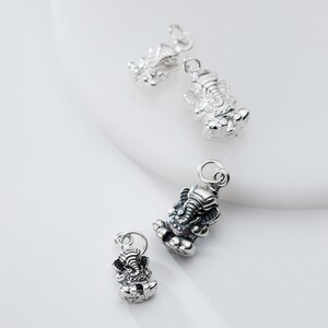 May include: Four silver charms in the shape of the Hindu deity Ganesha, an elephant-headed god. The charms are of varying sizes and are shown on a white background.