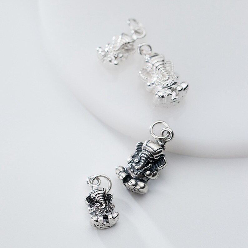 May include: Four silver charms in the shape of the Hindu deity Ganesha, an elephant-headed god. The charms are of varying sizes and are shown on a white background.