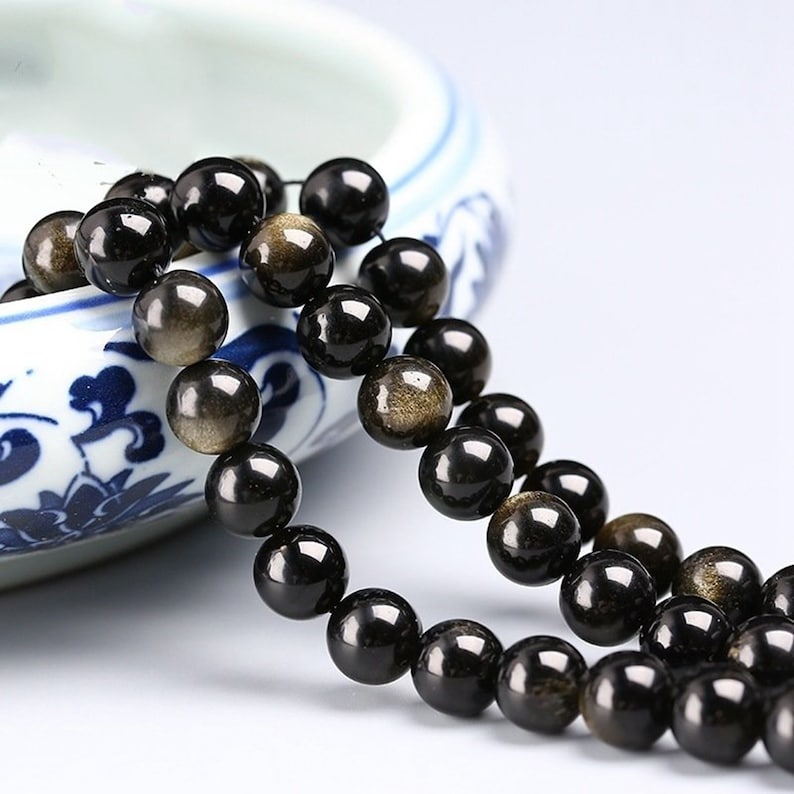 May include: A strand of black beads with gold flecks. The beads are round and smooth, and they are strung on a clear thread.