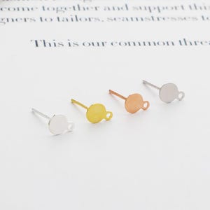 May include: Four earring post backs with a round disc and a small loop. The discs are silver, gold, and rose gold.